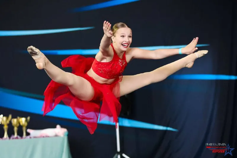Спортсменка в красном костюме в прыжке-шпагате на сцене